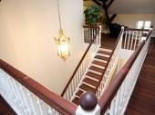 Representative Treppenanlage, bestehend aus geradeläufiger Holzwangentreppe und umlaufender Galerie. Wangen, Geländer und Setzstufen weiß deckend endbehandelt, Trittstufen und profilierter Handlauf (H 3) in Jatoba natur geölt. Geländer mit gedrechselten Stäben M 52, alle Pfosten gedrechselt mit Naturholzkugel